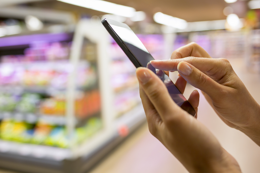A woman using her smartphone to buy groceries while in-store.